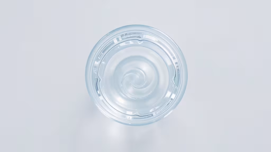 Verre d'eau cristalline vue de haut avec légère spirale dynamisant l'eau, lumière naturelle douce