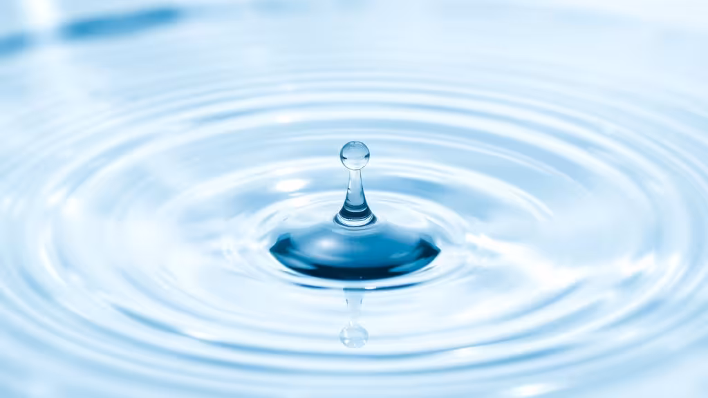Goutte d'eau tombant dans une surface claire avec reflets lumineux, évoquant la pureté et la vitalité de l'eau vivante